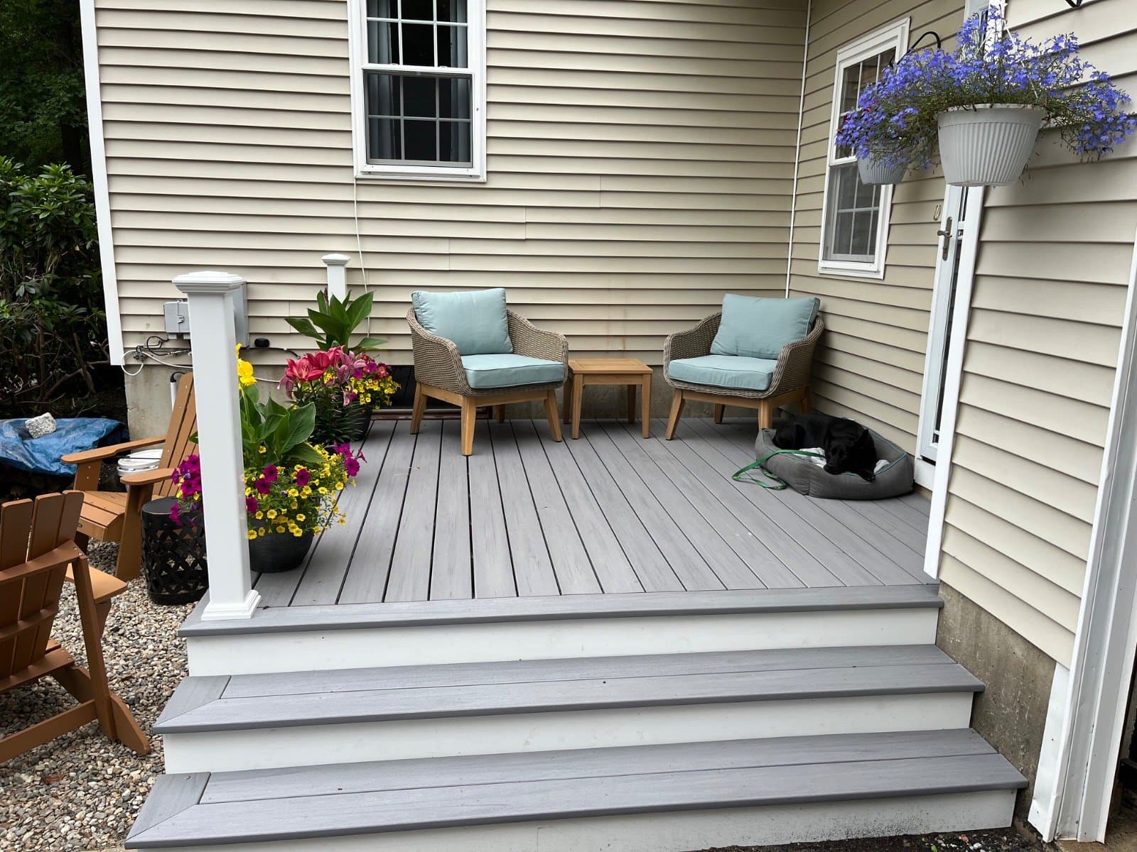 Finished side-entry composite deck styled with woven chairs, side table, planters of flowers, and a dog resting in the corner