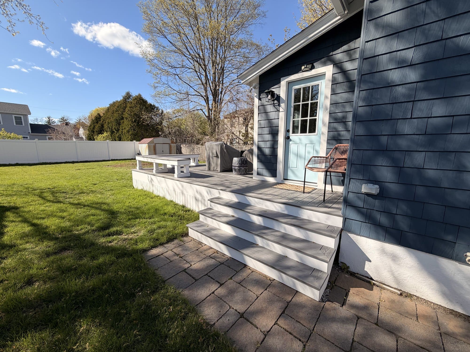 Finished composite deck with bench seating and a chair beside the cottage's blue back door, golden afternoon light