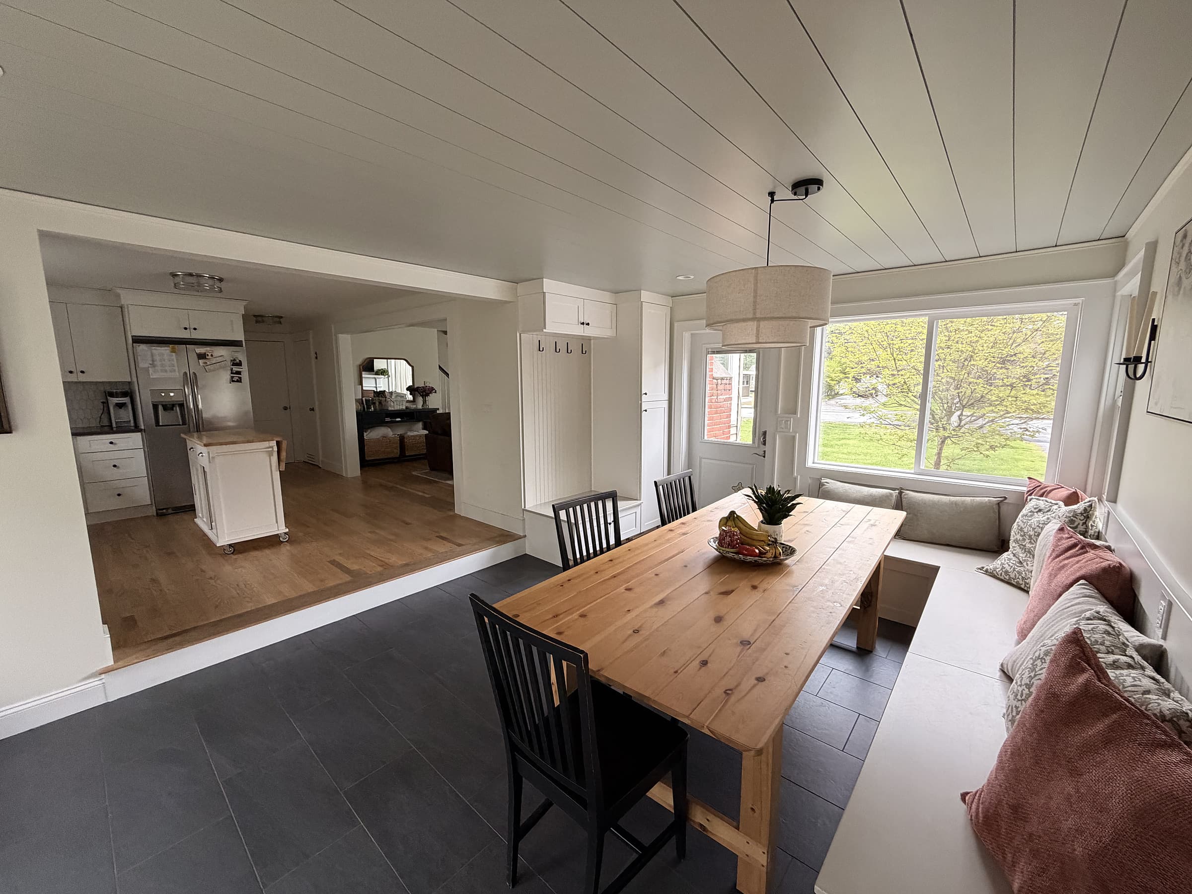 Finished dining room with shiplap ceiling, custom built-in bench seating, dining table, pendant light, and open view through to the kitchen