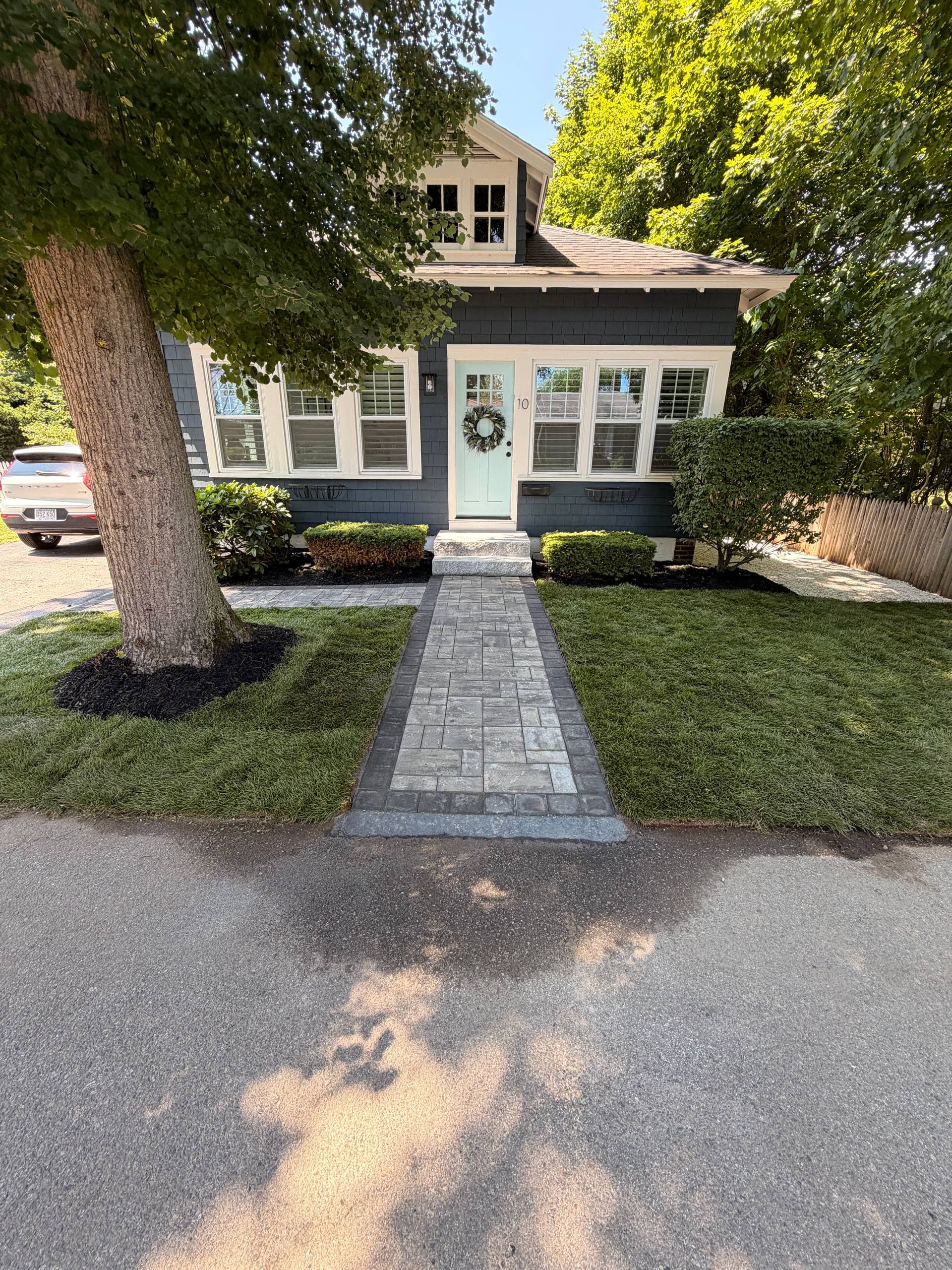 Finished front entry from the street — new gray paver walkway with granite steps leading to the door, framed by fresh sod and mulched beds